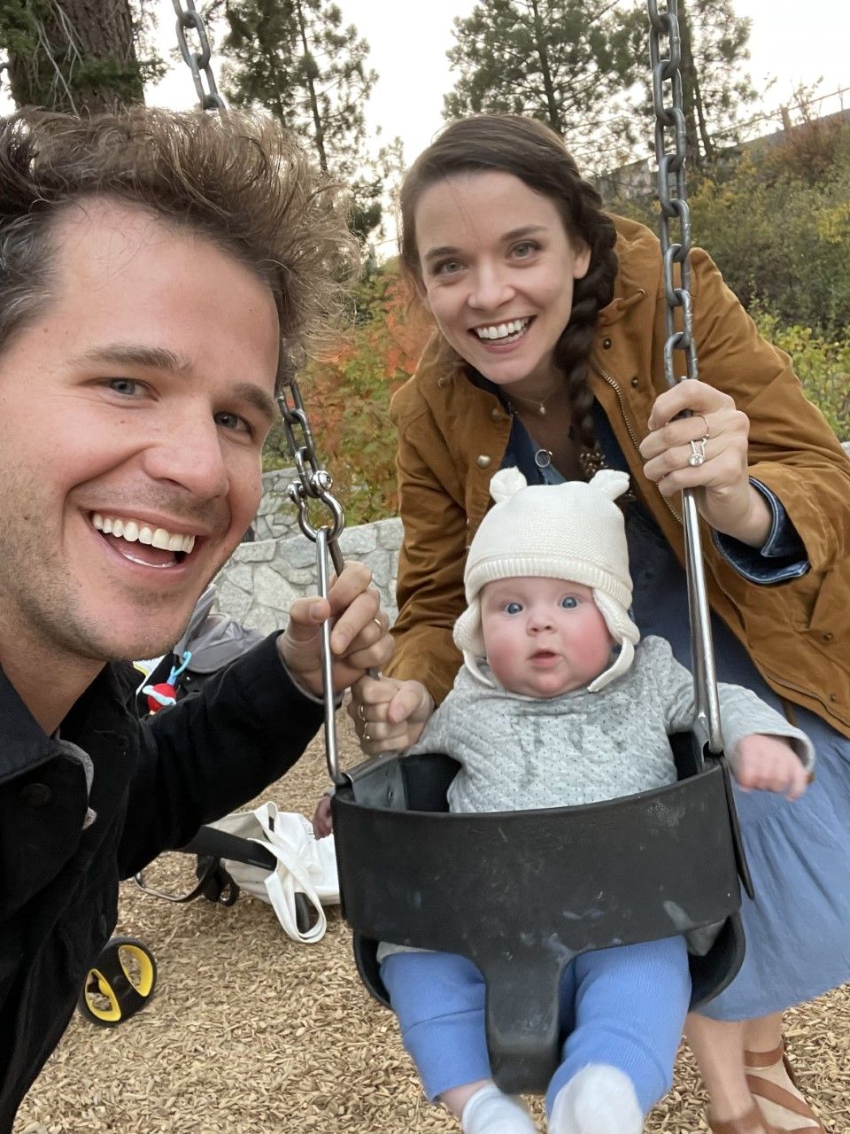 carly leahy with her husband charlie and their baby tavie sitting in a swing