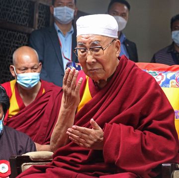 dalai lama with his eyes closed holding up his right hand while praying
