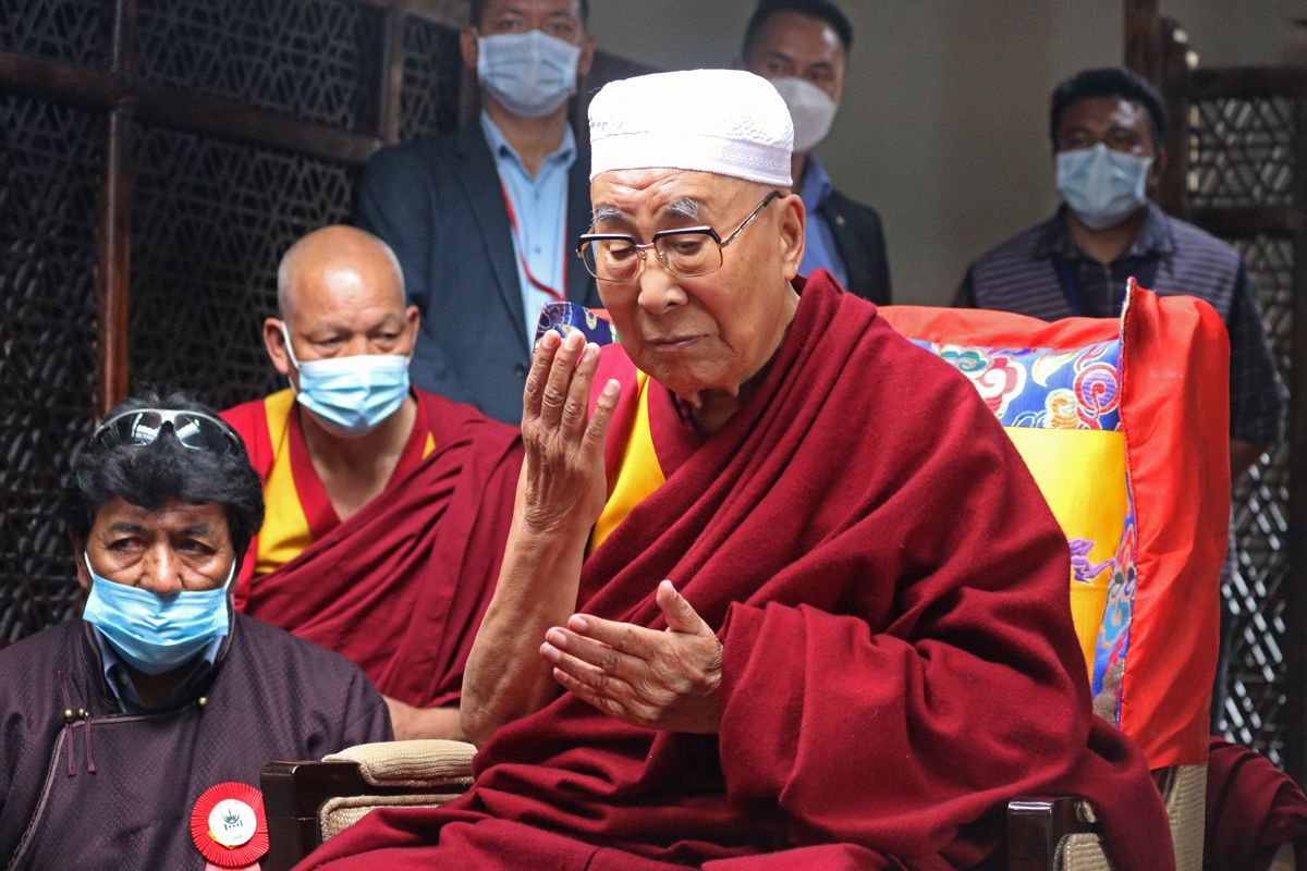 dalai lama with his eyes closed holding up his right hand while praying