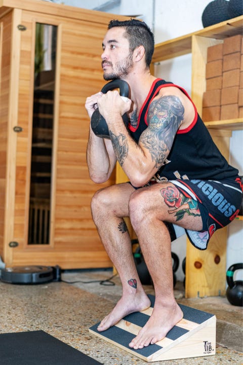 a man does a kettlebell squat using a slant board