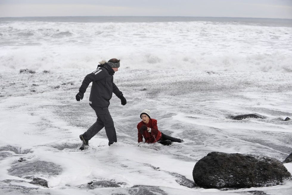 Een bejaarde toeriste wordt overvallen door een hoge golf op het strand Reynisfjara