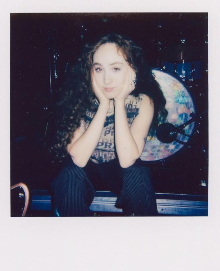 a person sitting on a stage with hands clasped under their chin featuring a drum set in the background
