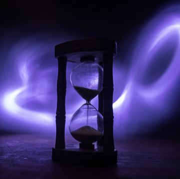 time concept silhouette of hourglass clock and old vintage wood clock with arrow and smoke on dark background with hot yellow orange red blue cold back lighting, or symbols of time with copy space