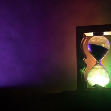 time concept silhouette of hourglass clock and smoke on dark background with hot yellow orange red blue cold back lighting, or symbols of time