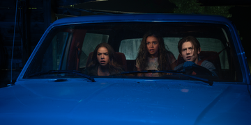 Interior of a vehicle with three people seated inside illuminated by blue light