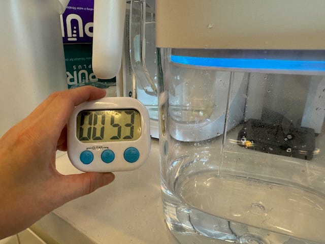 a hand holding a timer with water filtering into a pitcher