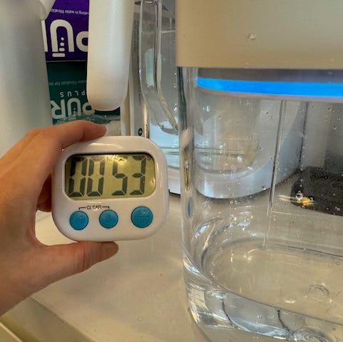 Best water filter pitcher a hand holding a timer with water filtering into a pitcher