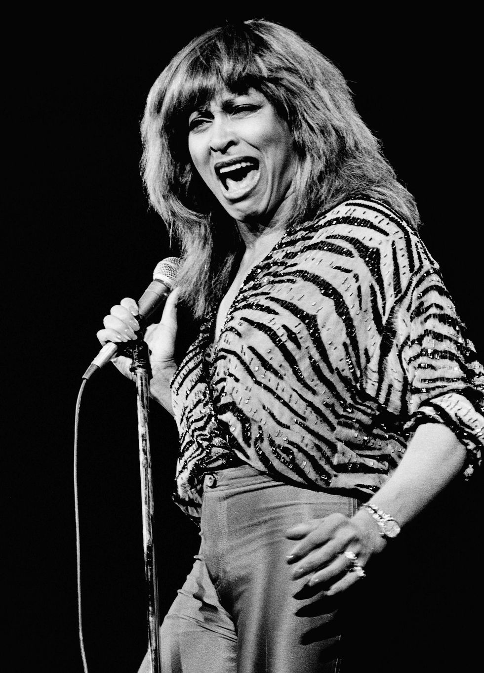 tina turner sings as she grips a microphone on a stand with one hand