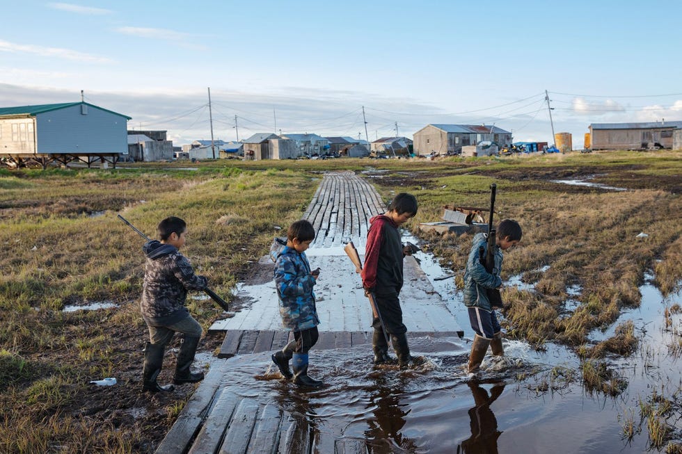 Het 380 inwoners tellende dorpje Newtok in Alaska verzakt steeds verder door het ontdooien van de permafrost waarop het is gebouwd Vier jongens van het Joepikvolk van links naar rechts Kenyon Kassaiuli Jonah Andy Larry Charles en Reese John steken een ondergelopen vlonderpad over