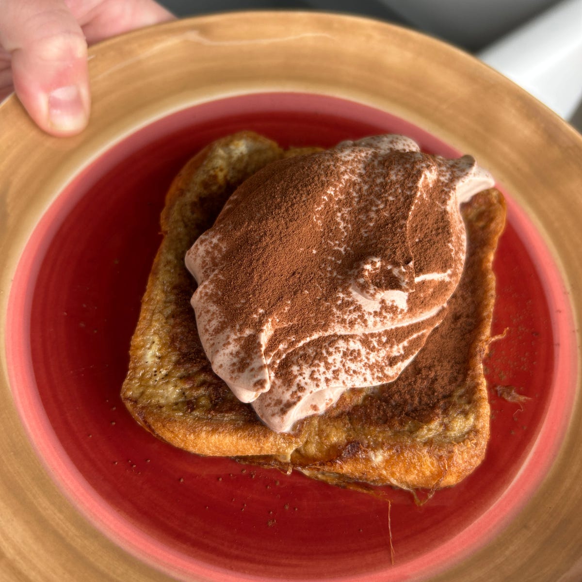 dessert featuring a slice of french toast topped with whipped cream and cocoa powder on a plate