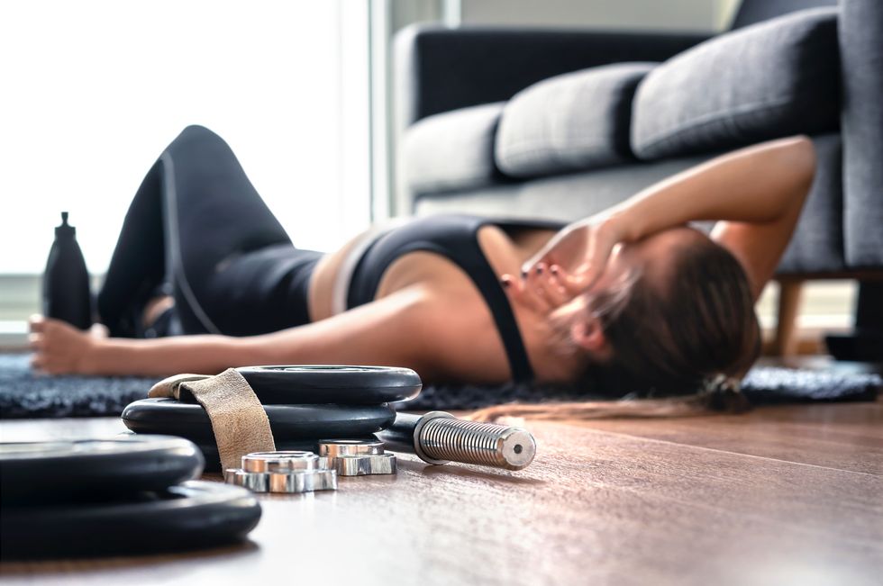 tired after exercise and workout overtraining concept exhausted woman lying on floor breathing and resting after heavy cardio training in home gym sad fitness athletet