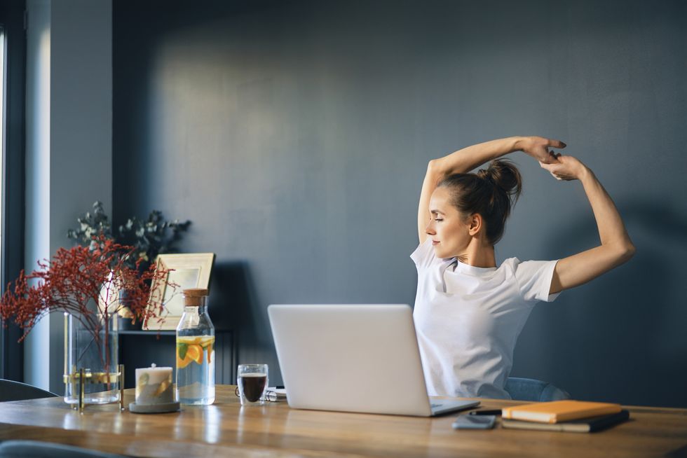 tired businesswoman stretching arms while sitting at desk in home office