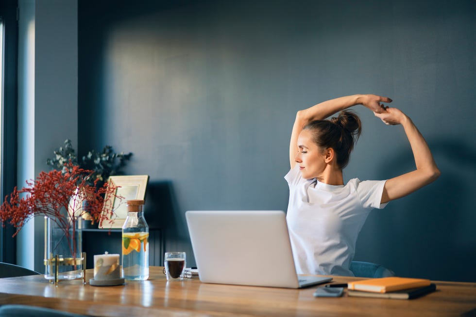 tired businesswoman stretching arms while sitting at desk in home office