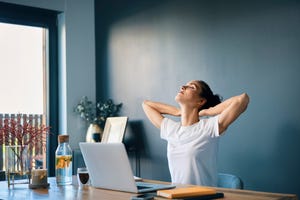 tired businesswoman with hands behind head sitting at desk in home office