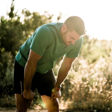 tired male runner bending in forest