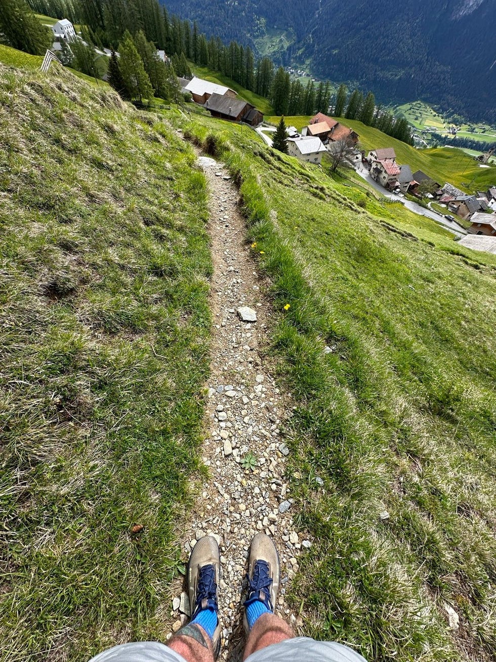 trail view from a persons feet overlooking a mountainous landscape with buildings