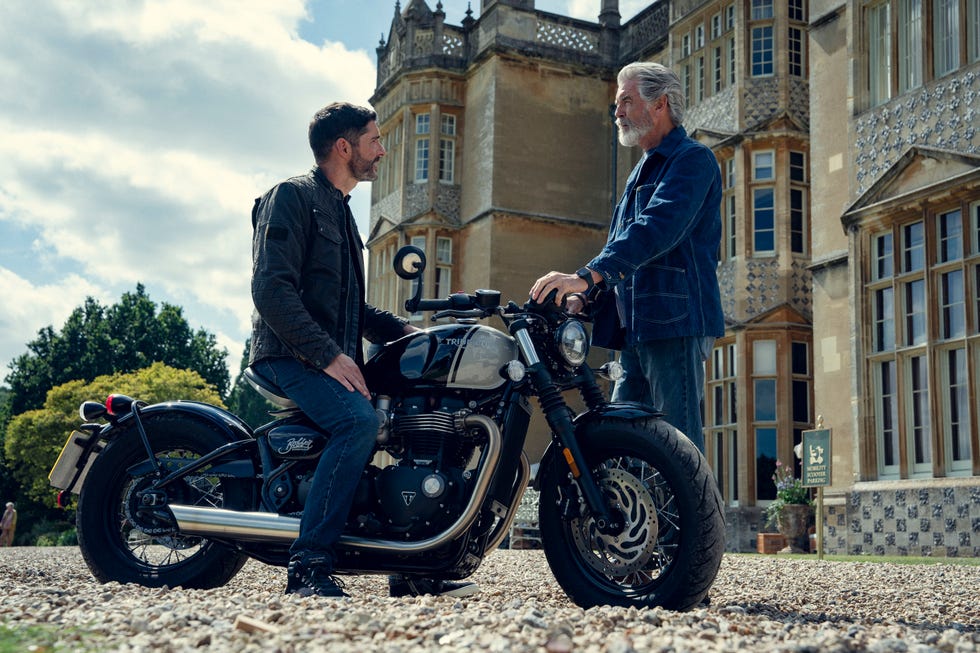two men discussing near a motorcycle in front of a historic building