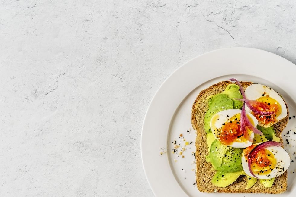 toast with boiled eggs and avocado on a plate on white background