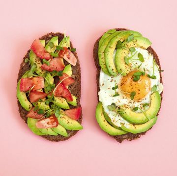 toasts of dark bread with avocado slices, red tomatoes, fried egg and microgreen. top view with pink background.