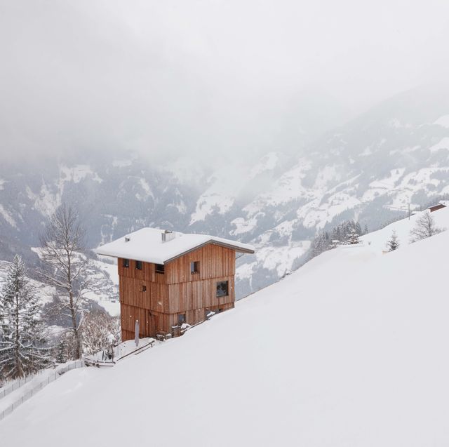 small isolated timber cabin on a snow covered hill surrounded by mountains