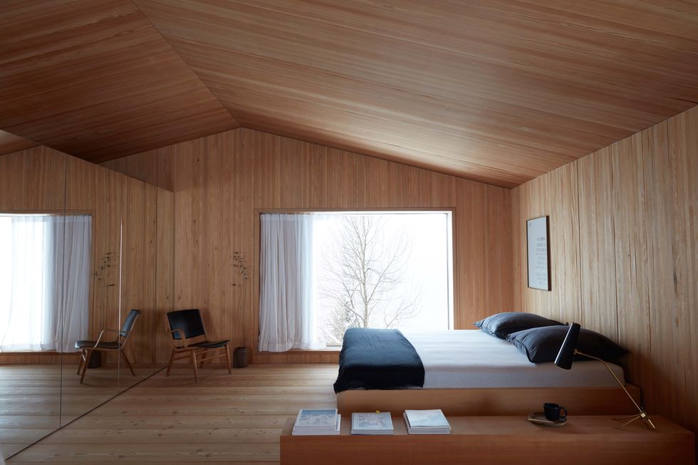 a minimal wood clad bedroom with a simple bed, pitched roof, and view of a tree out a large window