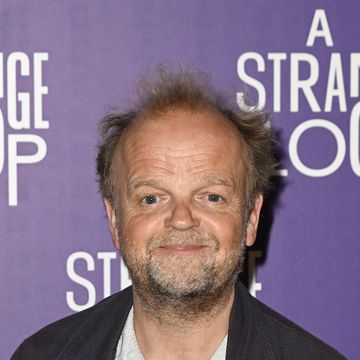 toby jones, an older man stands smiling at the camera, he has brown hair, wears a white shirt with jeans and black jacket