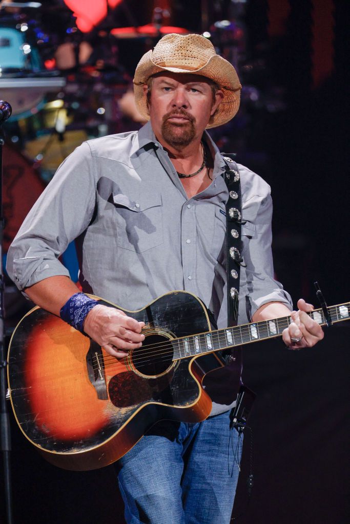 toby keith holding and playing a guitar while he performs onstage