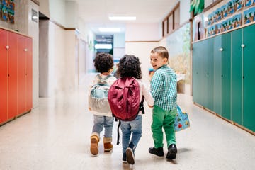 toddlers with backpacks walking down school hallway