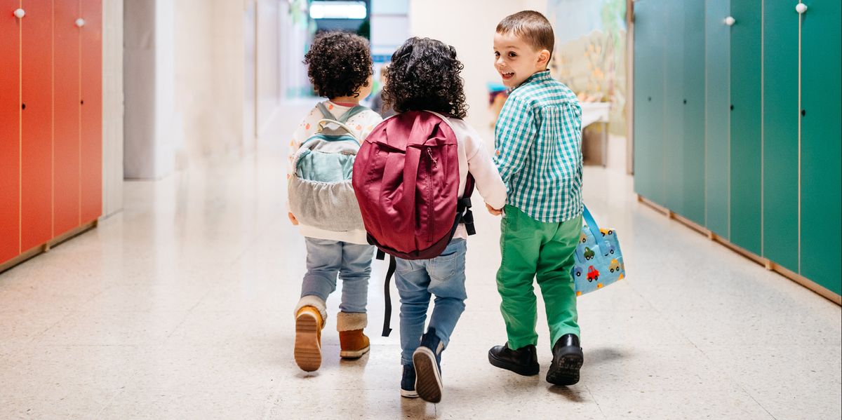 toddlers with backpacks walking down school hallway