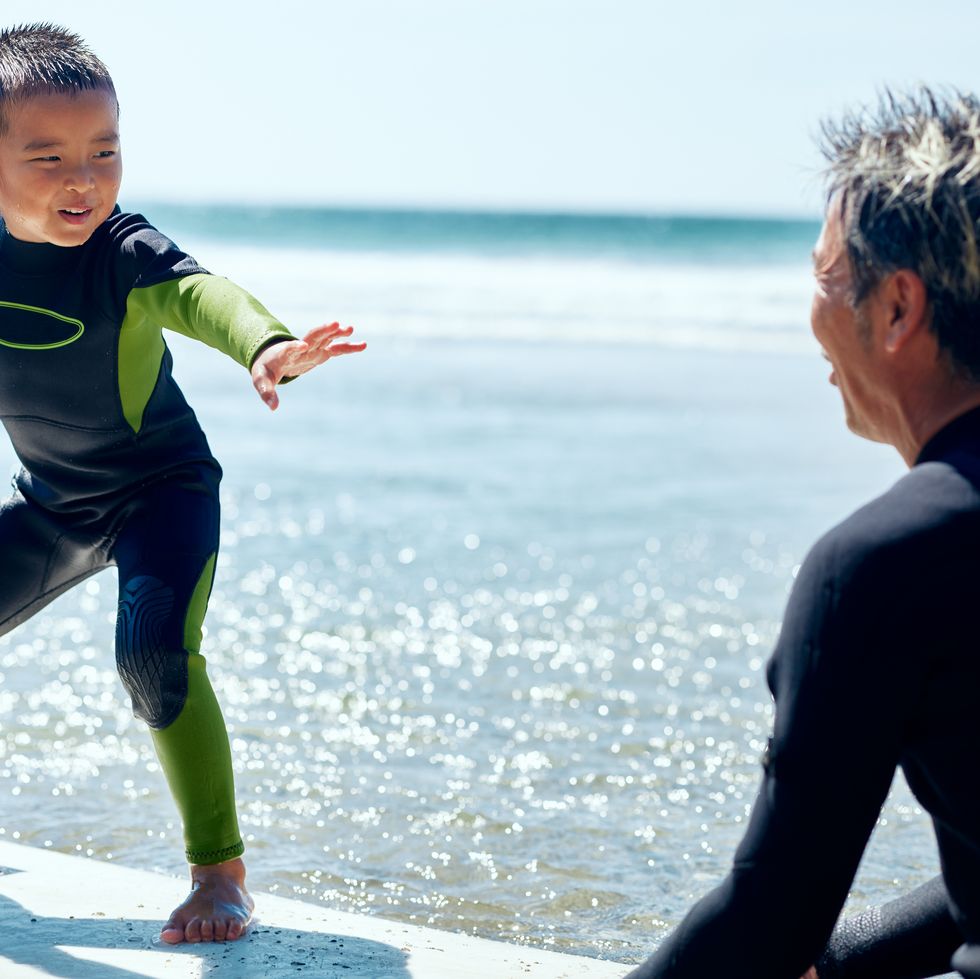 toddler experiencing surfing for the first time and his father watching over him