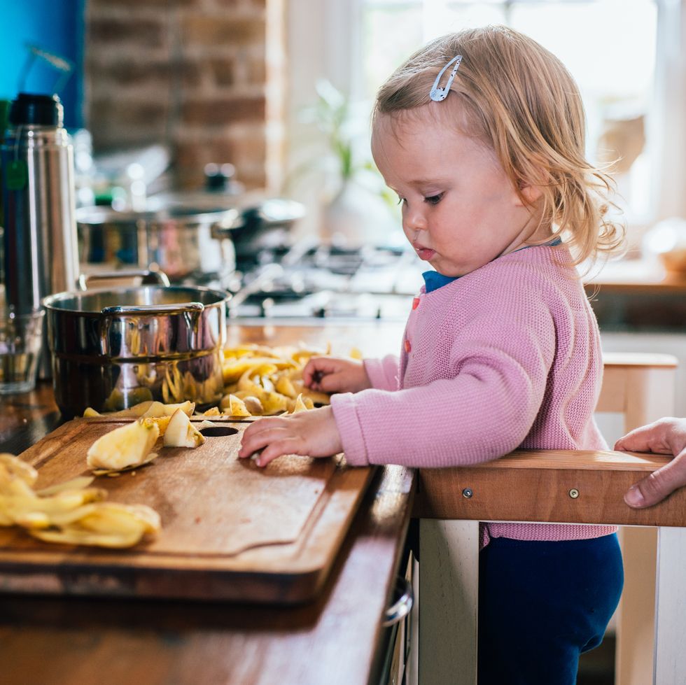 toddler girl looking at potato in kitchen while preparing food with her mother.