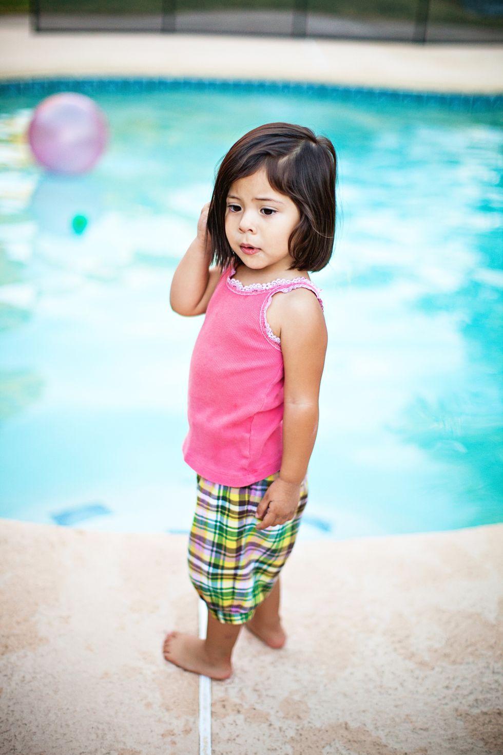 una niña vestida con camiseta y pantalón corto en el borde de una piscina