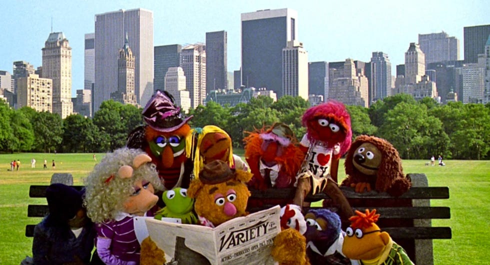 the muppets gather around a newspaper in a scene from the muppets take manhattan, a good housekeeping pick for best toddler movies