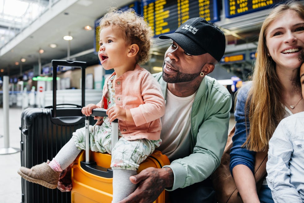 toddler sits on suitcase while waiting for flight with family