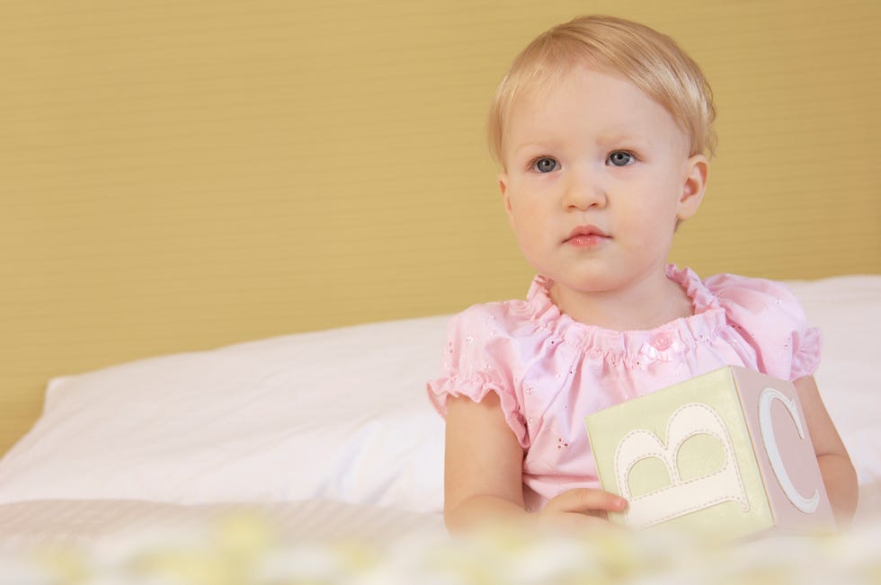 toddler sitting up in bed playing with alphabet blocks