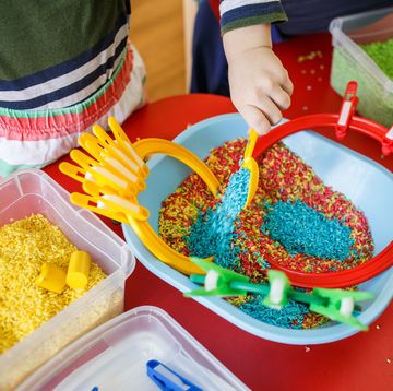toddlers playing with sensory bin with colourful rice on red table