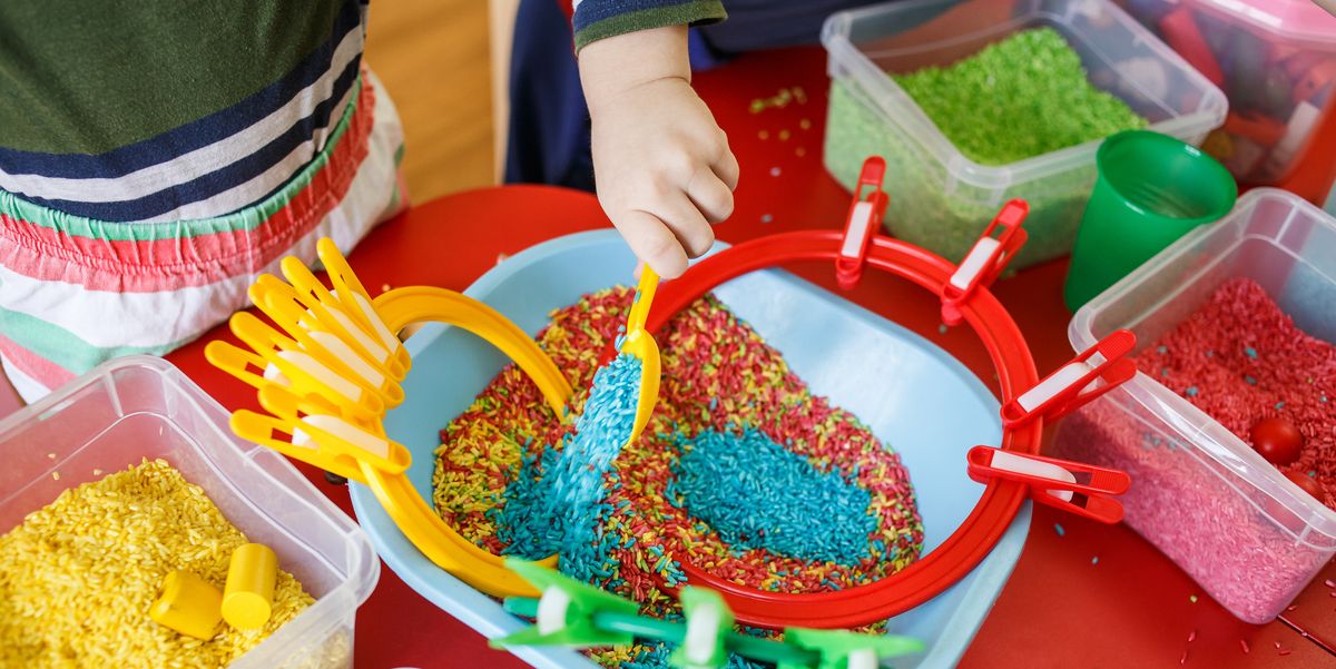 toddlers playing with sensory bin with colourful rice on red table