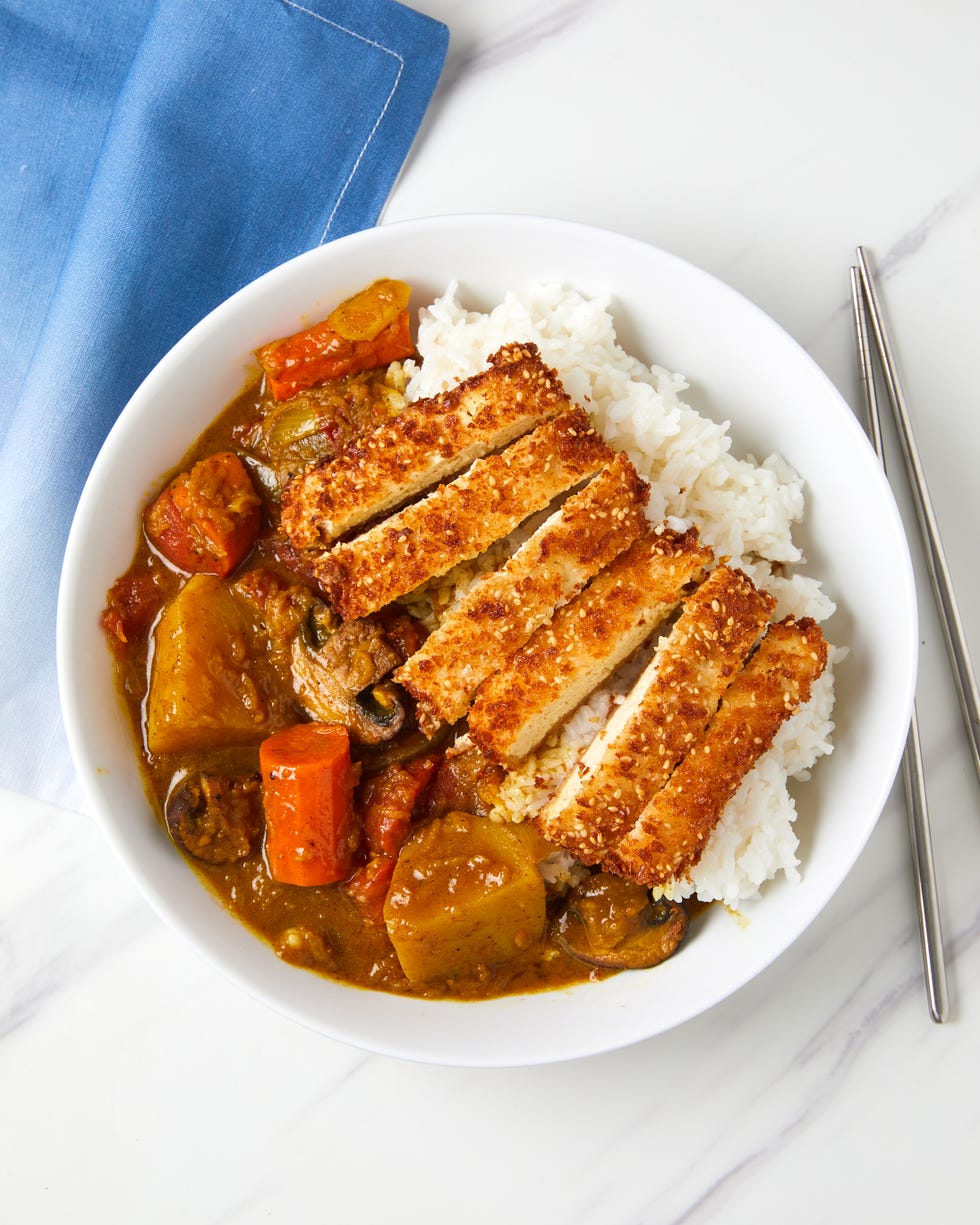 white rice, sesame panko crusted tofu, tender vegetables, and a rich and flavorful curry sauce in a white bowl
