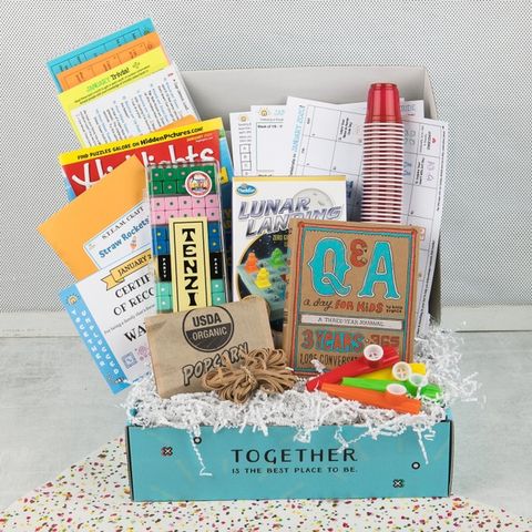 blue box that reads together is the best place to be and is filled with white crinkle paper and lots of childrens activities like a highlights magazine lunar landing game and q and ​a booklet