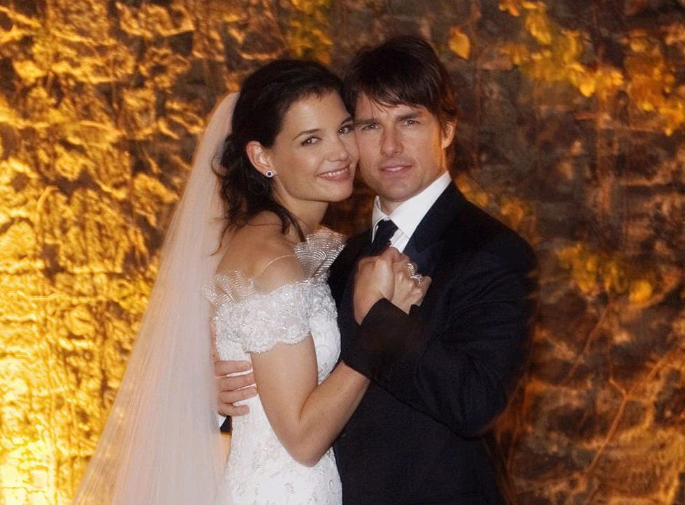 katie holmes in a wedding dress and veil hugs tom cruise in a black suit and tie as they hold hands