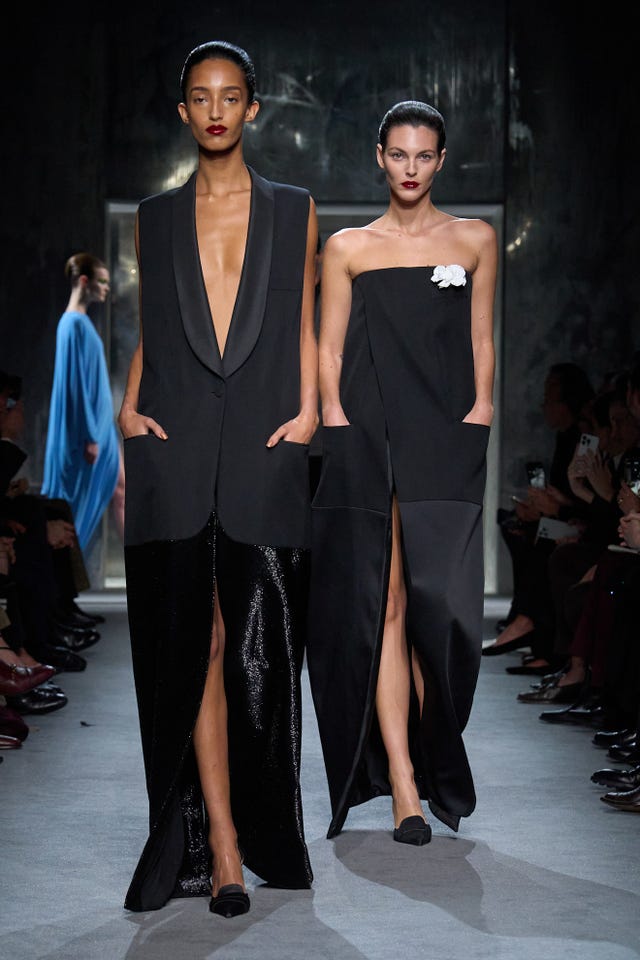 Fashion runway presentation featuring two models in stylish dark attire