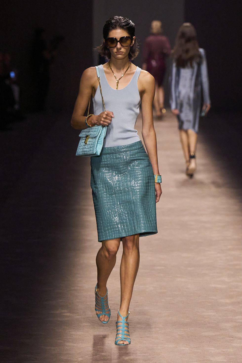 a woman wearing a blue dress and sunglasses walking on a runway
