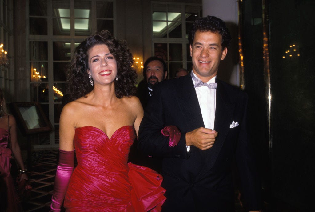 rita wilson and tom hanks smiles as they walk together in formal attire