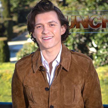 tom holland smiling, wearing a white shirt and brown suede jacket