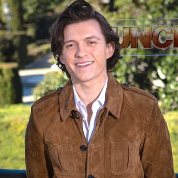 tom holland smiling, wearing a white shirt and brown suede jacket