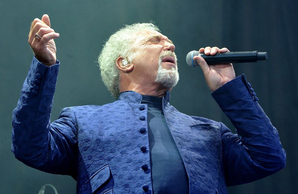 tom jones singing into a microphone, wearing a black shirt and blue jacket
