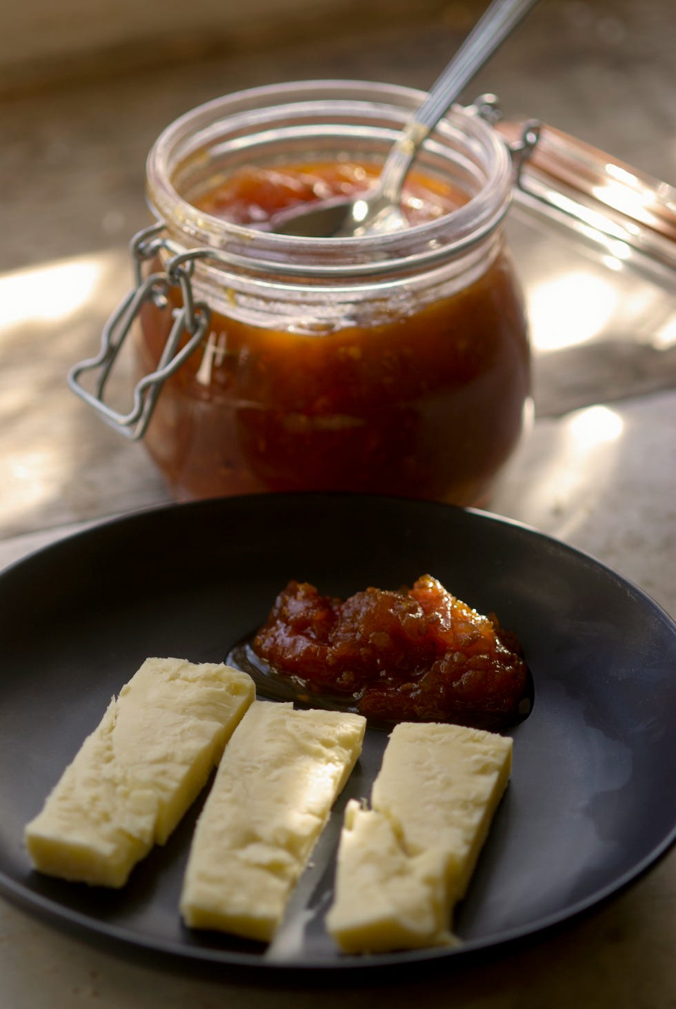 Tomato and chilli relish in a jar and served with cheddar cheese on a plate, close-up