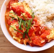 stir fried tomato and egg with white rice in a white bowl against a light wood background