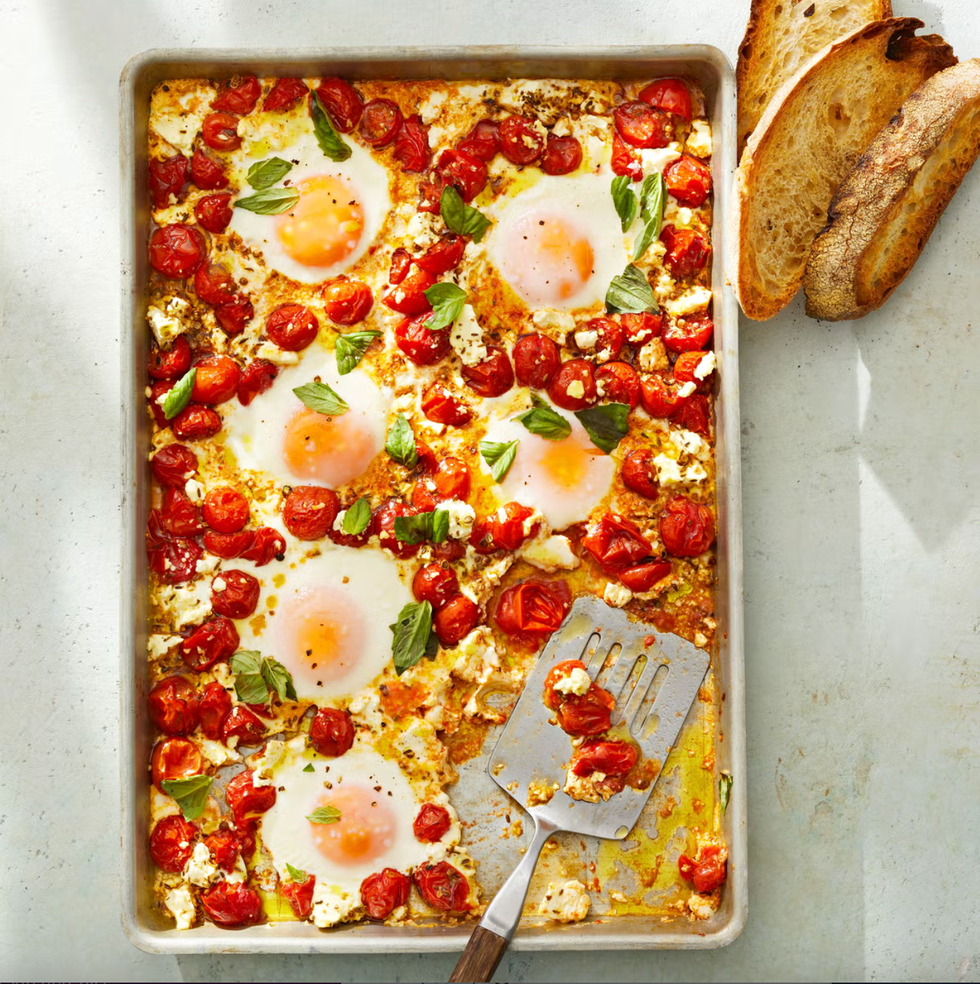 tomato and feta baked eggs on a sheet pan with a metal spatula