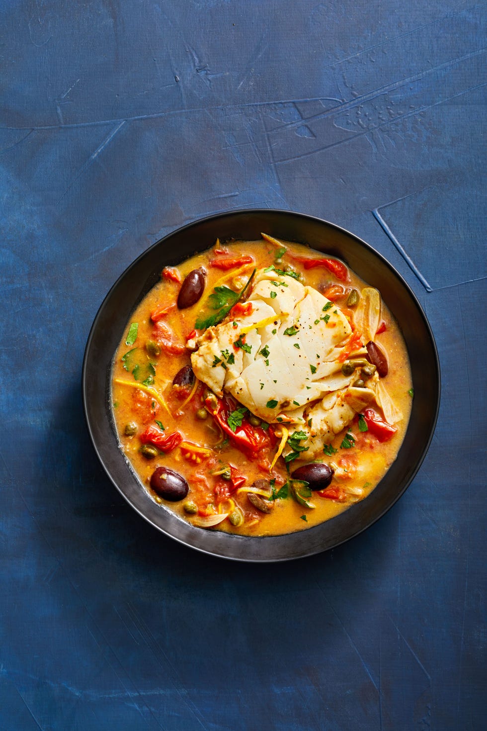 tomato poached cod with olives and capers in a black bowl